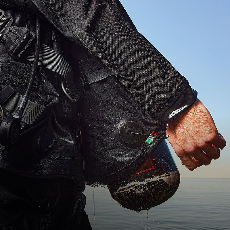 Overpressure relief valve mounted on a drysuit sleeve, with pull cord and colored tab visible