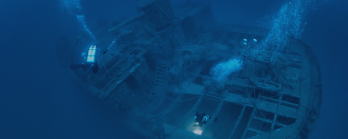Two divers exploring a sunken shipwreck underwater with air bubbles rising